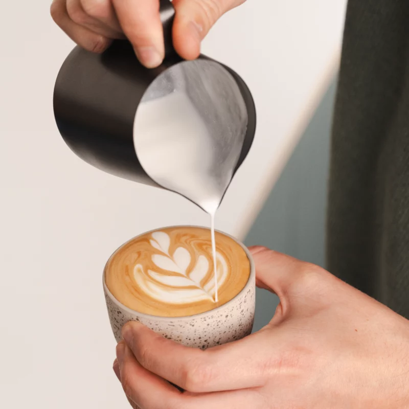 Barista creating latte wart with foam from a  Stainless Steel Milk pitcher latte art Essentials 600ml black